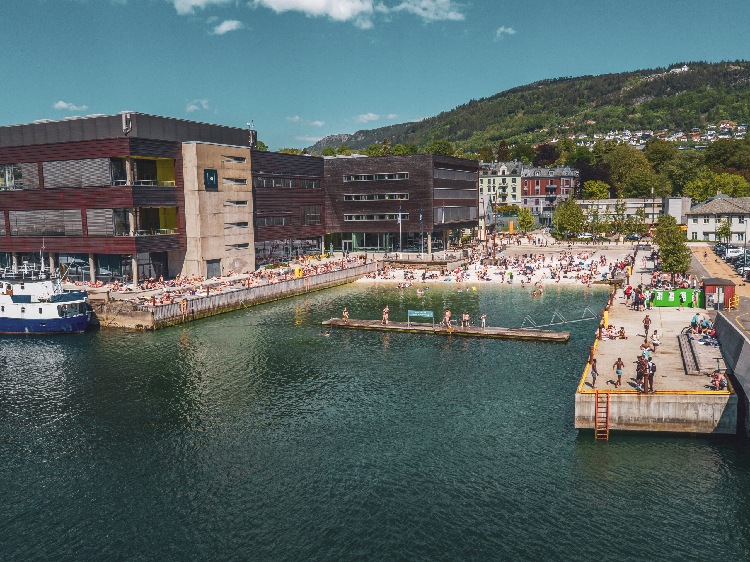 Dronefoto over Marineholmen bystrand en solskinnsdag. Mange bader og koser deg.